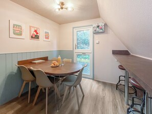 A dining area with a wooden table and four chairs, a small bar counter, and a window with a view of greenery. - A lovely lodge in a great holiday village. (Kingsdown, Deal)