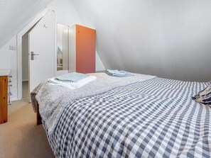 A bedroom with a checkered bedspread, a fluffy white blanket, and a folded towel. There is a door leading to a hallway with a mirror and a red cabinet. - A lovely lodge in a great holiday village. (Kingsdown, Deal)