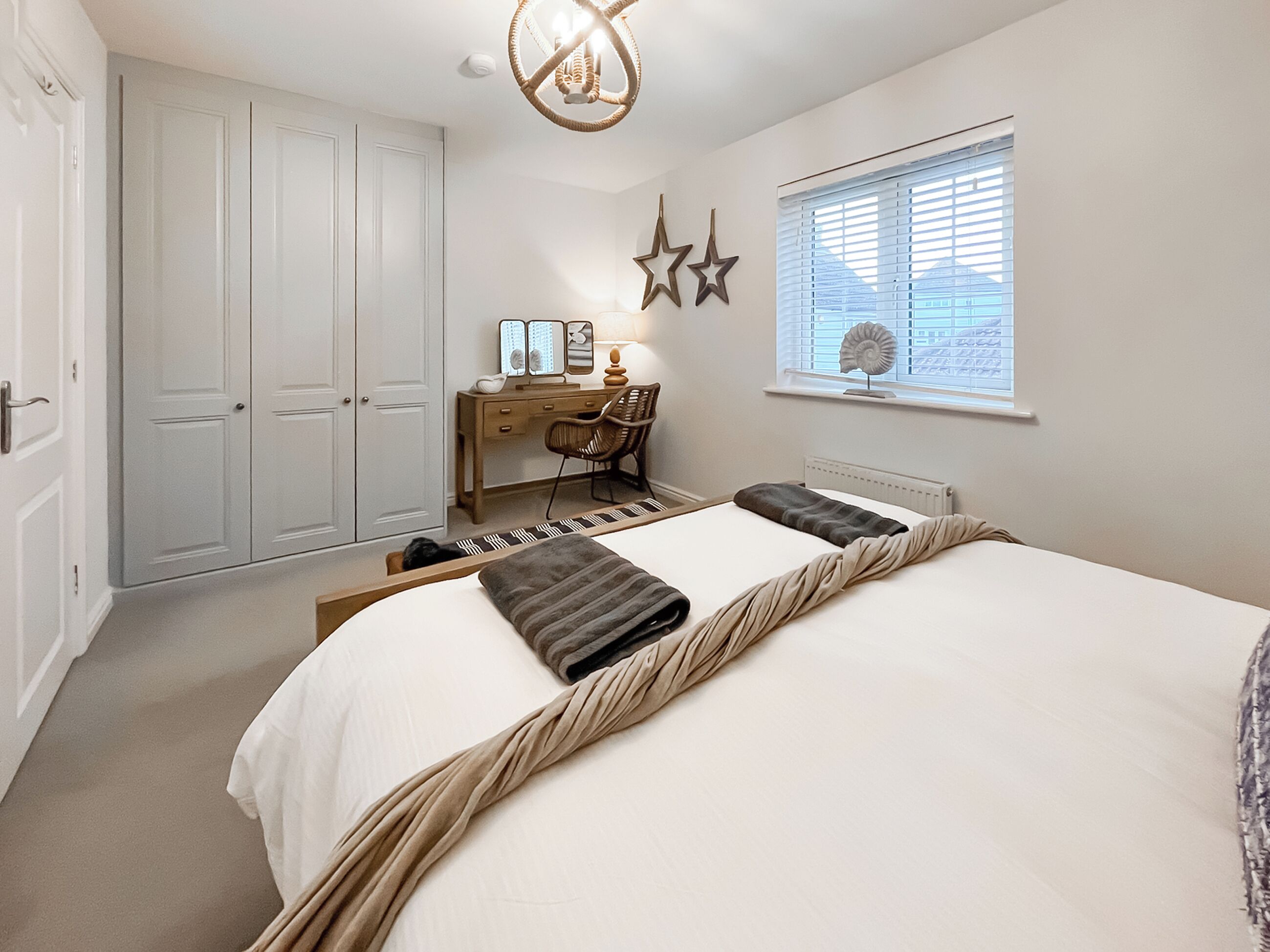 A bedroom with a bed, a desk, a chair, a wardrobe, and a window with blinds.