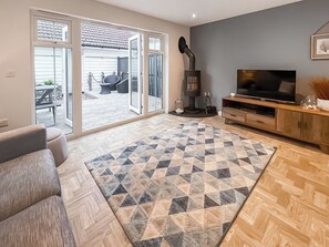 Ein Wohnzimmer mit Sofa, Fernseher, Kamin und Blick auf die Terrasse.