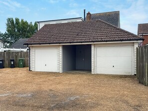 Ein eingeschossiges Gebäude mit Ziegeldach, zwei Garagentoren und einem umzäunten Garten.