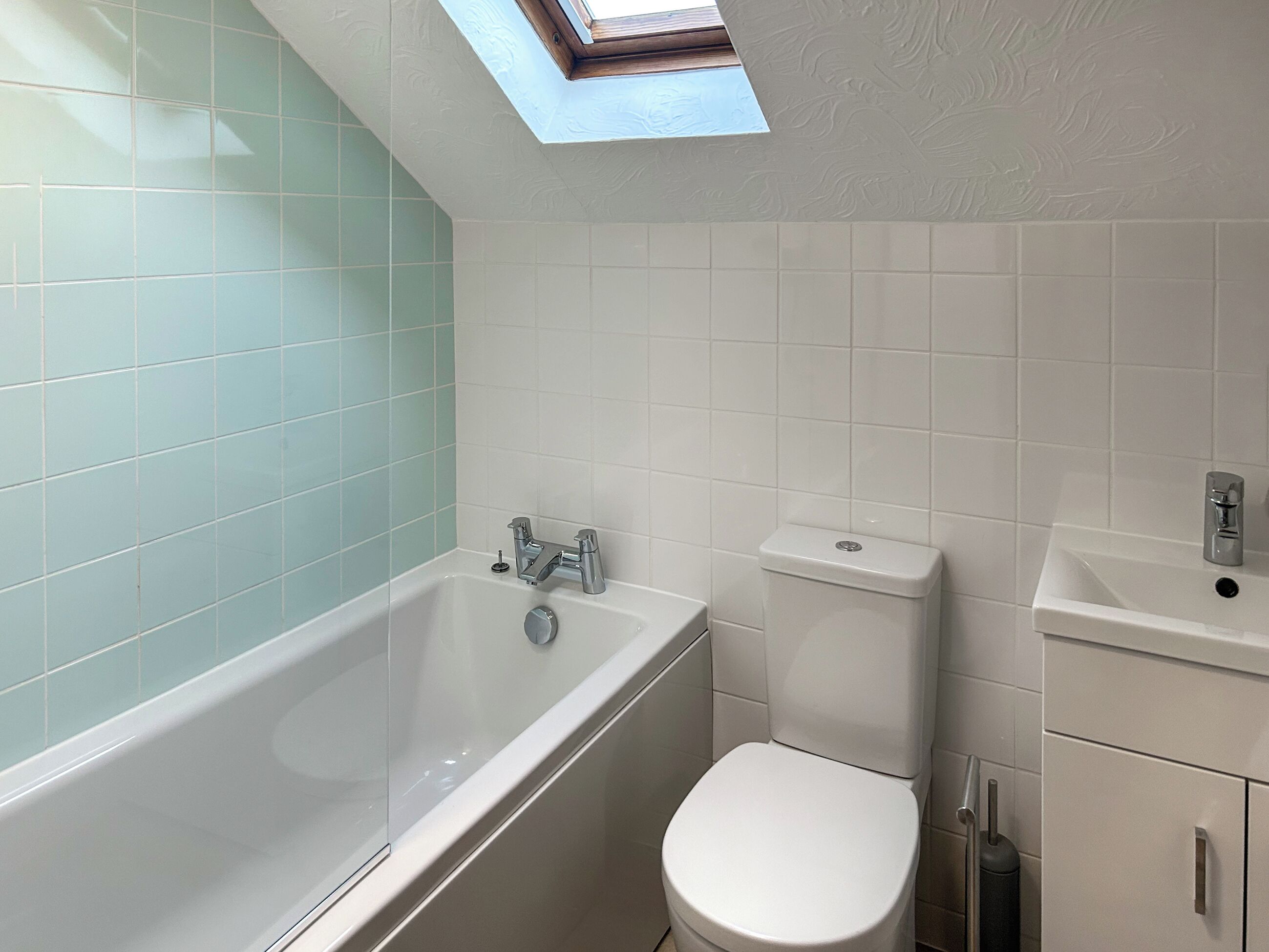 A bathroom with a skylight, a bathtub, a toilet, and a sink.