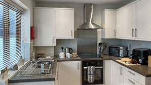 Moderni keittiö, jossa on valkoiset kaapit, ruostumattomasta teräksestä valmistettu liesituuletin, sisäänrakennettu uuni, mikroaaltouuni ja leivänpaahdin.