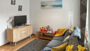 Olohuoneessa on harmaa sohva, puinen kaappi, televisio ja seinällä taulu.