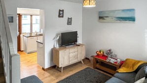 Olohuone, jossa on televisio, puinen kaappi ja taulu, jossa on kuvattuna ranta.