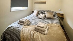 A bedroom with a bed, pillows, a window with a blind, and a bedside table.