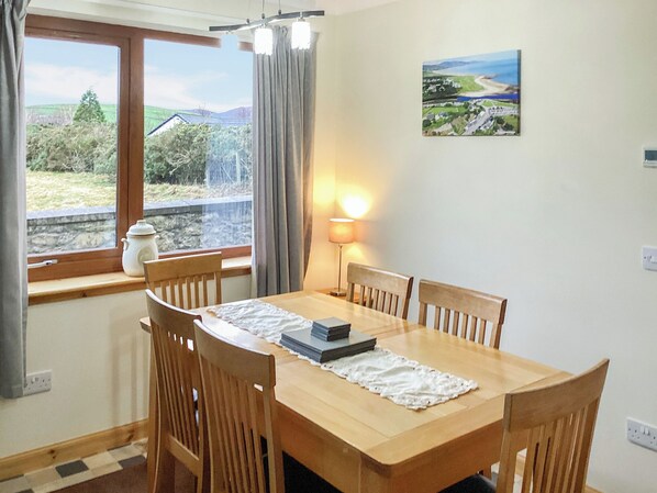 A dining room with a wooden table, six chairs, a lamp, a window with curtains, and a landscape painting on the wall.