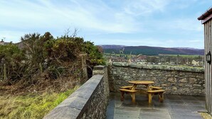 A stone wall with a wooden table and benches, overlooking a rural landscape with houses and hills. - 4 bedroom accommodation in Brora (Brora)