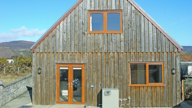 A wooden building with a gabled roof, two large windows, and a door. - 4 bedroom accommodation in Brora (Brora)