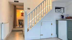 A staircase with white railings, a chair in the background, and a kitchen area with appliances. - Mini Goose cottage - UKC7088 (Laycock)