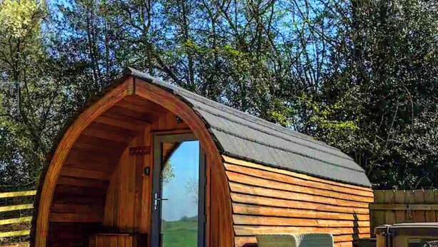A wooden structure with an arched roof, a door, and a small porch area. - The Orchard - UKC7804 (Shrewsbury)