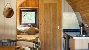 A cozy cabin with a wooden interior, a bed with pillows, a dining table, and a kitchen area. - The Orchard - UKC7804 (Shrewsbury)