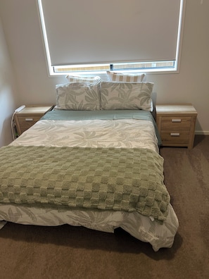 Ein Schlafzimmer mit einem Bett, zwei Nachttischen, einem Fenster und Teppichboden.