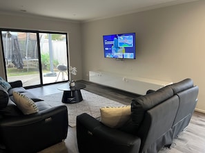 Ein modernes Wohnzimmer mit einem schwarzen Ledersofa, einem runden Couchtisch und einem flachbildfernseher, der an der Wand befestigt ist.