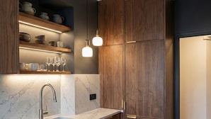 Una cucina moderna con mobili in legno, piani in marmo, forno integrato e illuminazione a sospensione.