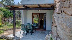 A covered patio with a table and chairs, a stone wall, and a door leading inside. - Beautiful apartment for 4 guests with A/C, WIFI, pool, TV and pets allowed (Palau)