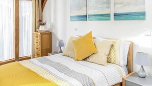 Een slaapkamer met een bed, een houten hoofdbord, een nachtkastje, een lamp, een dressoir en een raam met gordijnen.