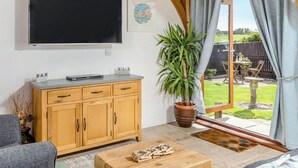 Een woonkamer met een televisie, een houten kast en een plant in pot.