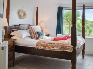 Una cama con dosel y tablero de madera, ropa blanca de cama y un plaid decorativo.