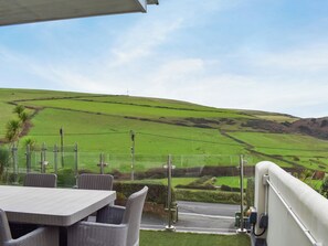Una terraza con mobiliario de mimbre con vistas a un paisaje verde, colinas onduladas y una carretera.