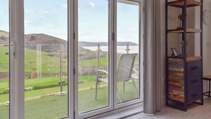 Et værelse med en stor skydedør, der fører ud til en balkon med udsigt over et grønt landskab og bakker.