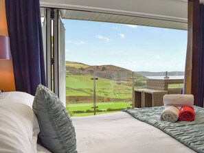 Ein Hotelzimmer mit großem Fenster und Blick auf grüne Hügel und ein Gewässer.