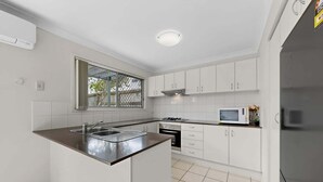 Een moderne keuken met witte kastjes, een roestvrijstalen spoelbak, een magnetron en een gasfornuis.