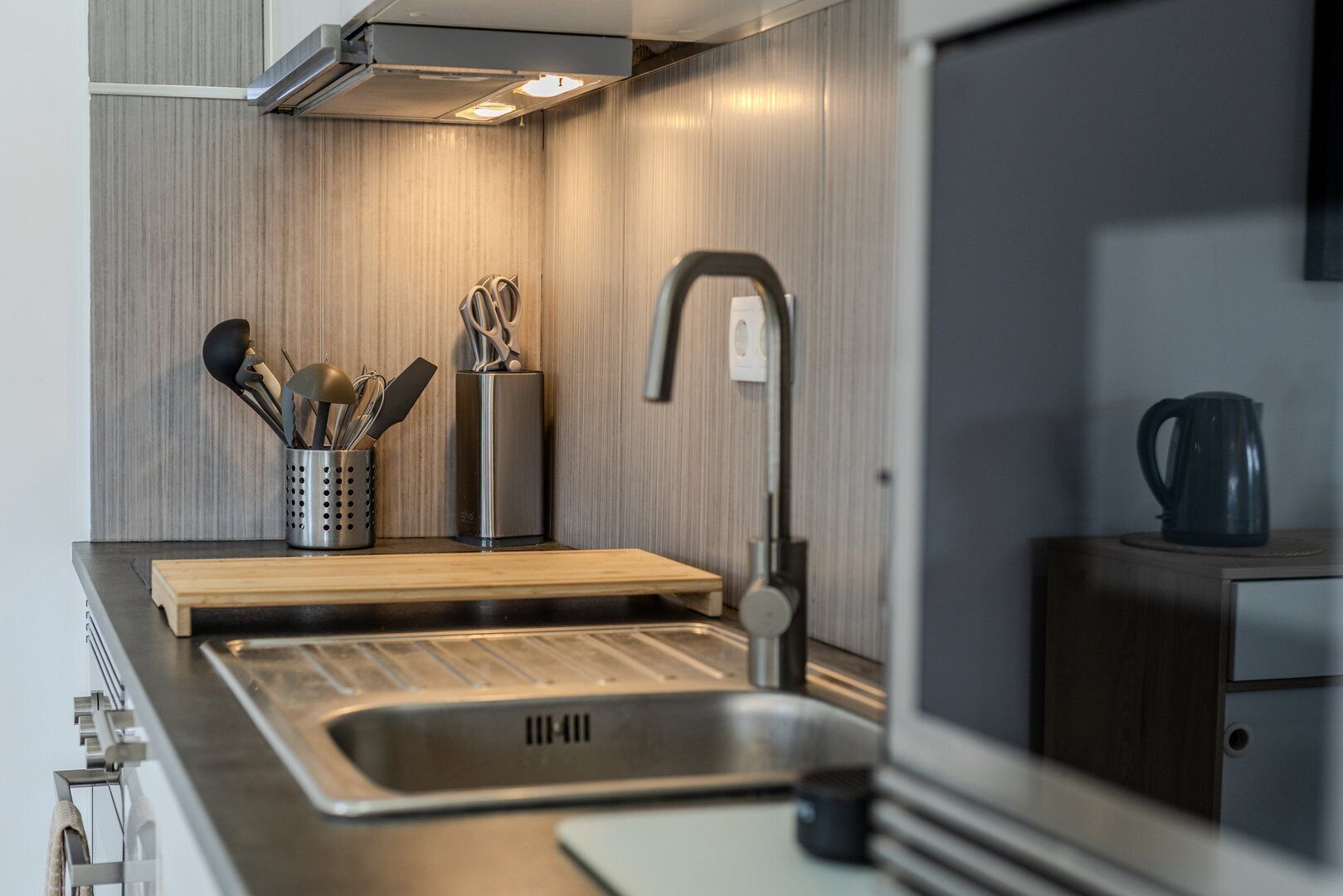 Eine moderne Küche mit einer Edelstahlspüle, einem Holzer Schneidebrett und einer Kaffeemaschine.