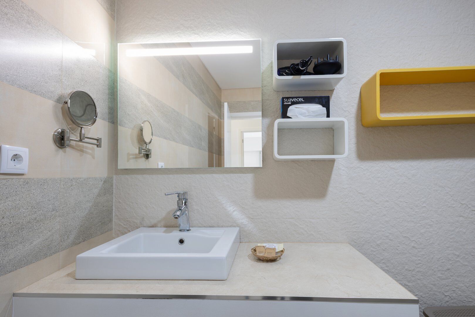 Un baño con un lavamanos rectangular, un espejo y una repisa con artículos de aseo.