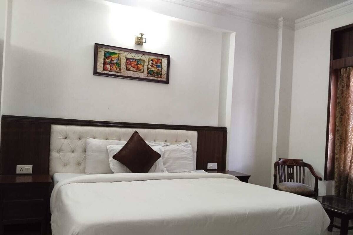 A neatly made bed with a headboard, a bedside table, a chair, and a wall-mounted picture.