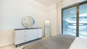 A modern bedroom with a bed, a dresser, a mirror, and a large window with a view of a building.