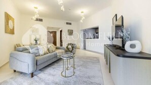 A modern living room with a grey sofa, a glass coffee table, and a small side table. There is a black console table with a mirror and a decorative plant. - 327 Bloomfields Magnificent 1BR Ajwan (Madinat Zayed)