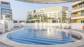 A swimming pool with lounge chairs, a covered area, and modern buildings with balconies.