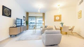 A modern living room with a sofa, a dining table with chairs, a TV on a cabinet, and artwork on the walls.