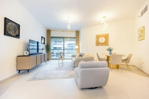 Una sala moderna con un sofá, una mesa de comedor con sillas, un televisor en un mueble bajo y obras de arte en las paredes.