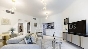A modern living room with a grey sofa, a round coffee table, and a flat-screen TV on a cabinet. - 327 Bloomfields Magnificent 1BR Ajwan (Madinat Zayed)