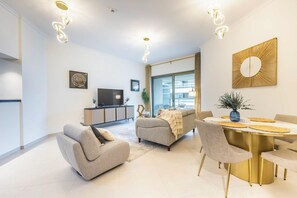 A modern living room with a dining area, a flat-screen TV, and a large window.