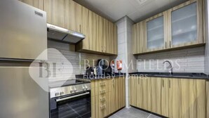 A modern kitchen with wooden cabinets, stainless steel appliances, and a tiled backsplash. - 327 Bloomfields Magnificent 1BR Ajwan (Madinat Zayed)