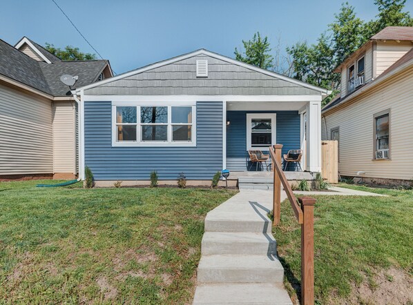 A single-story house with a front porch, a small front yard, and a visible satellite dish.