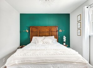 A bedroom with a wooden headboard, white bedding, and teal walls.