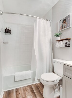 A modern bathroom with a glass shower enclosure, white tiles, a toilet, and a wooden floor.