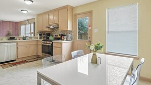 A modern kitchen with beige cabinets, a central island, and a dining area with a glass table. - 🎁 Holiday Savings! Modern 4-Bedroom Home in Katy• Game Area • Crib • Firepit (Katy)