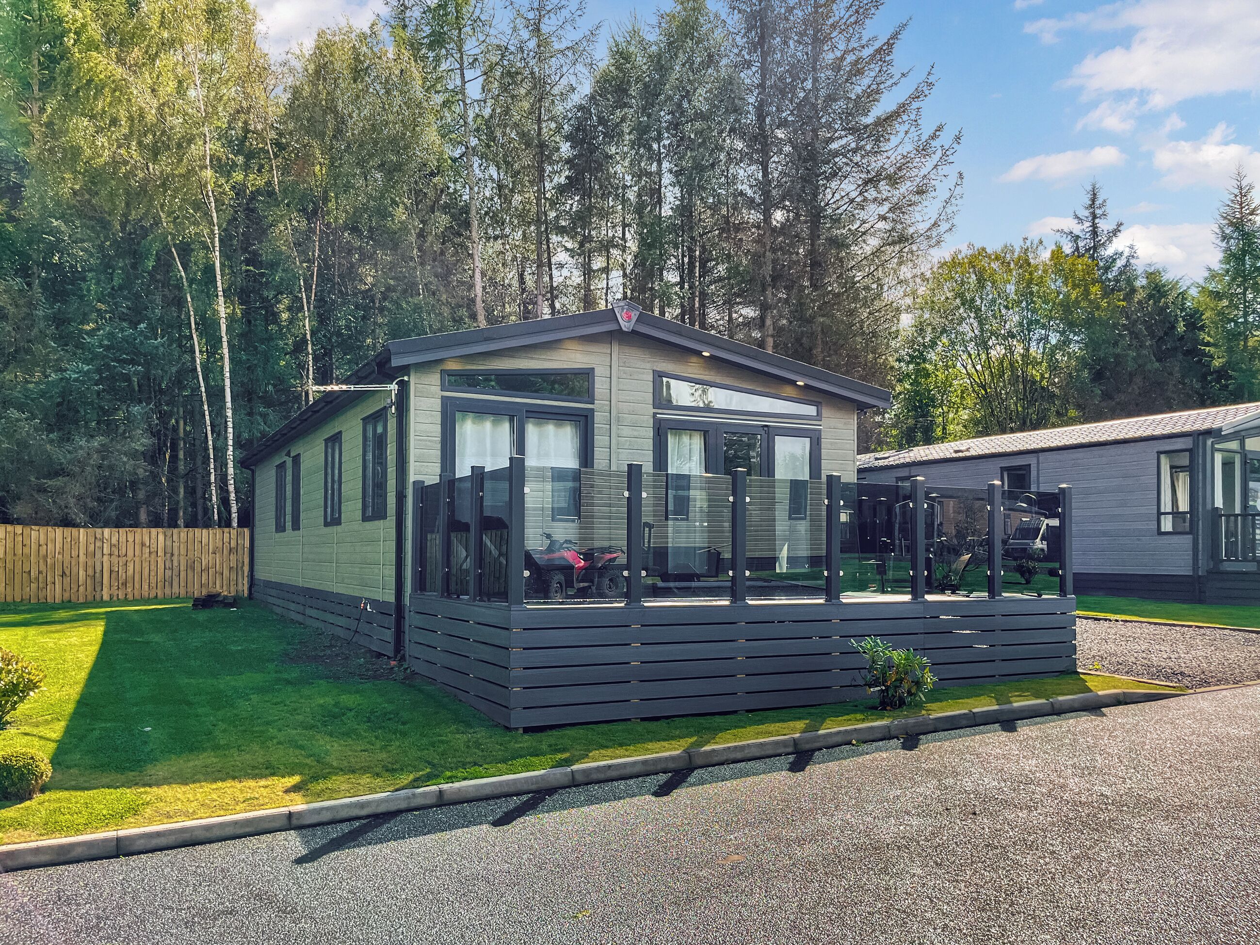 Une maison mobile moderne dotée d’une terrasse et d’un espace extérieur couvert, le tout entouré d’arbres.