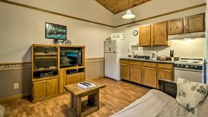 A compact kitchen with wooden cabinets, a refrigerator, a stove, and a dining area with a table and chairs. - Inviting Cabin Retreat with a Private Hot Tub in Bryson City, North Carolina (Bryson City)