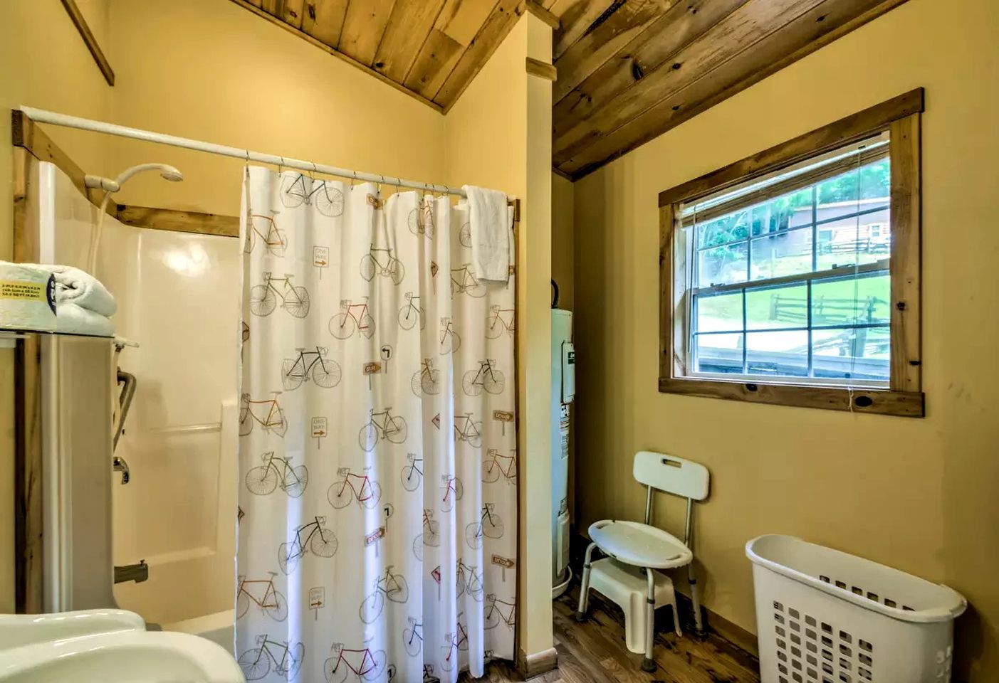 Un baño con ducha, inodoro, ventana con vistas y una cesta de ropa.