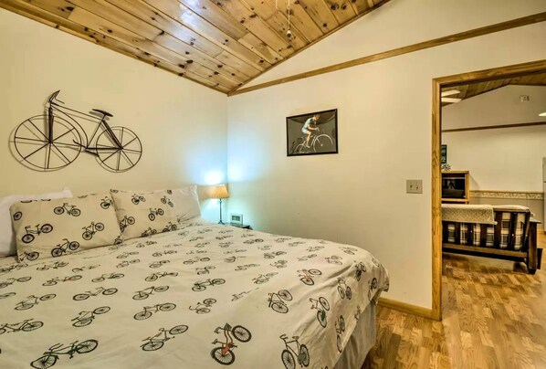 Un dormitorio con cama, ropa de cama con motivos de bicicleta, una decoración de bicicleta en la pared, un cuadro enmarcado y techo de madera.
