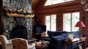 A rustic cabin interior with a stone fireplace, wooden furniture, and large windows. - Beautiful Log Cabin with Jacuzzi Bathtub in the heart of Adirondack State Park (Saranac Lake)