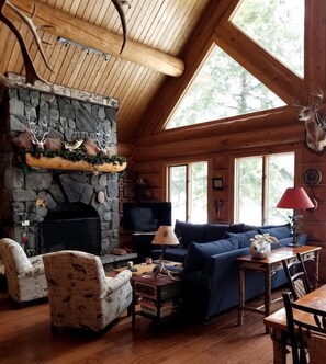 L’intérieur d’un chalet rustique, avec une cheminée en pierre, des meubles en bois et de grandes fenêtres.