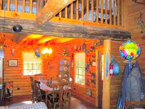Interior rústico de una cabaña con comedor, paredes de madera y una escalera.