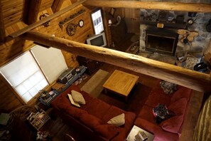 A cozy cabin interior with a stone fireplace, wooden beams, a red sofa, and a television. - Spacious and Rustic Cabin Rental in the Woods near Catoctin Mountain Park, Maryland (Thurmont)